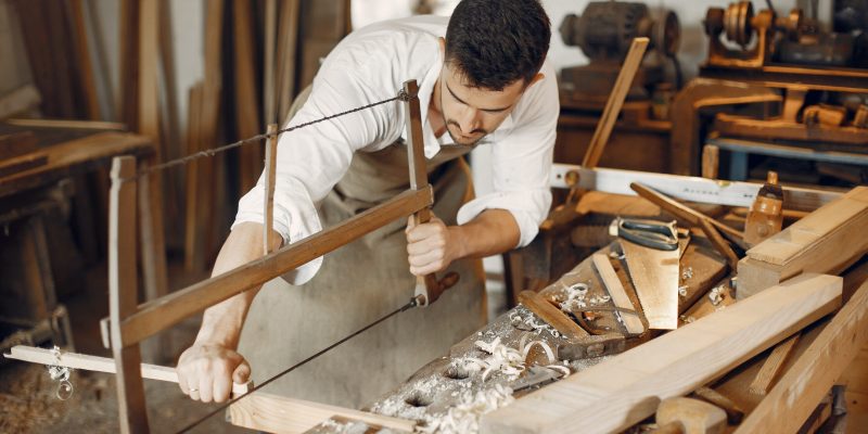 Man working with a wood. Carpenter in a white shirt